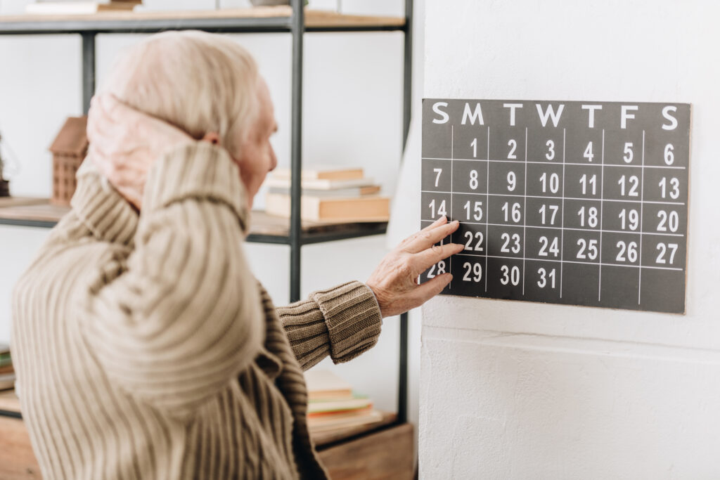 man with grey hair touching wall calendar and head